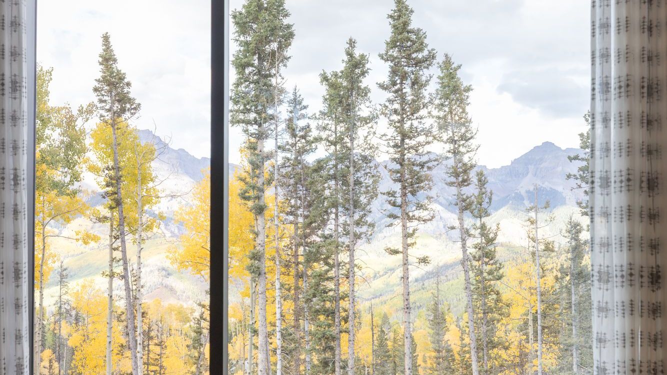 Gold aspens and evergreens framed by a large window with the San Juan Mountains beyond, fall in Telluride